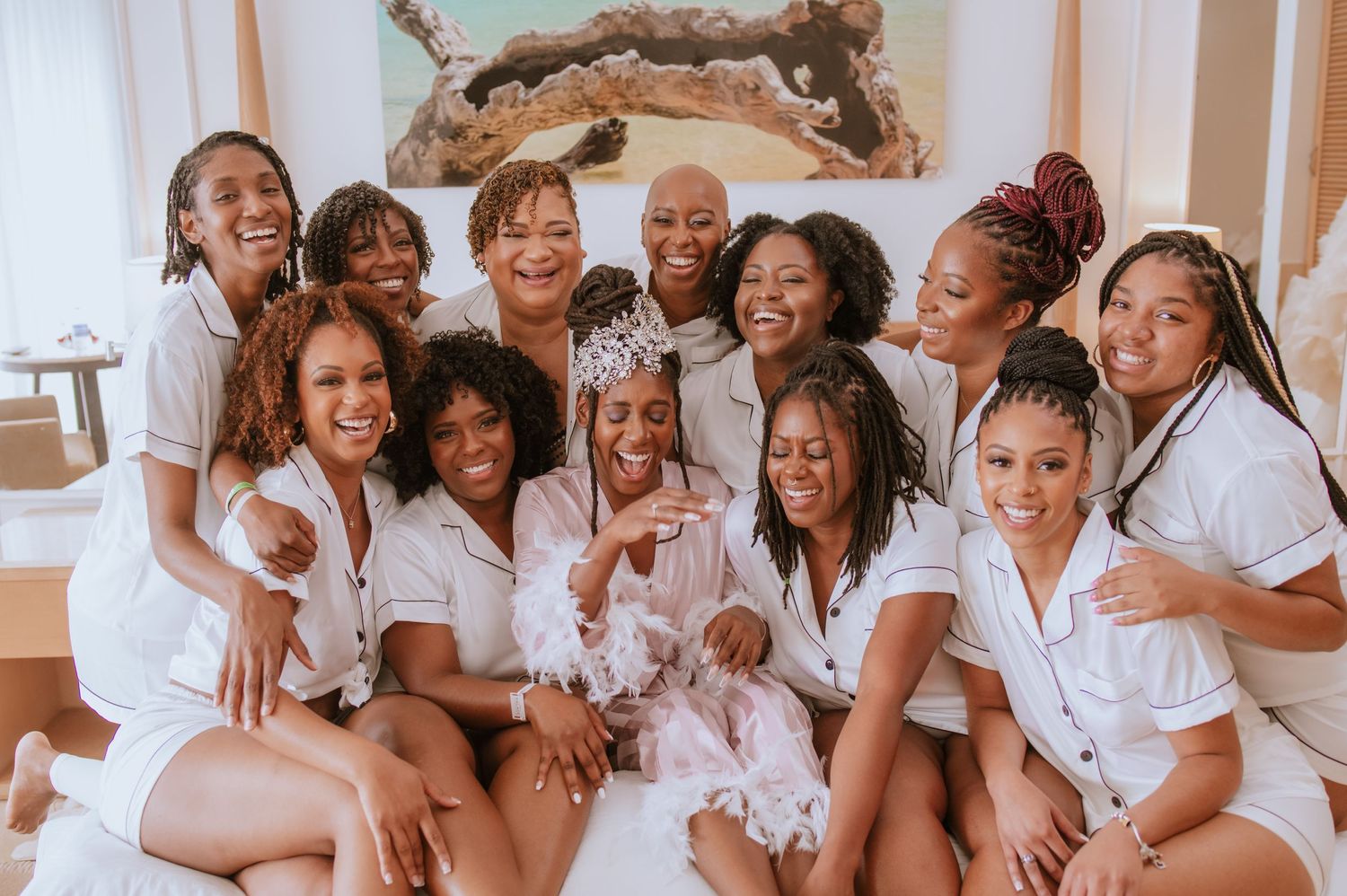Wedding party wearing matching white robes poses together on a bed during pre-ceremony preparations.