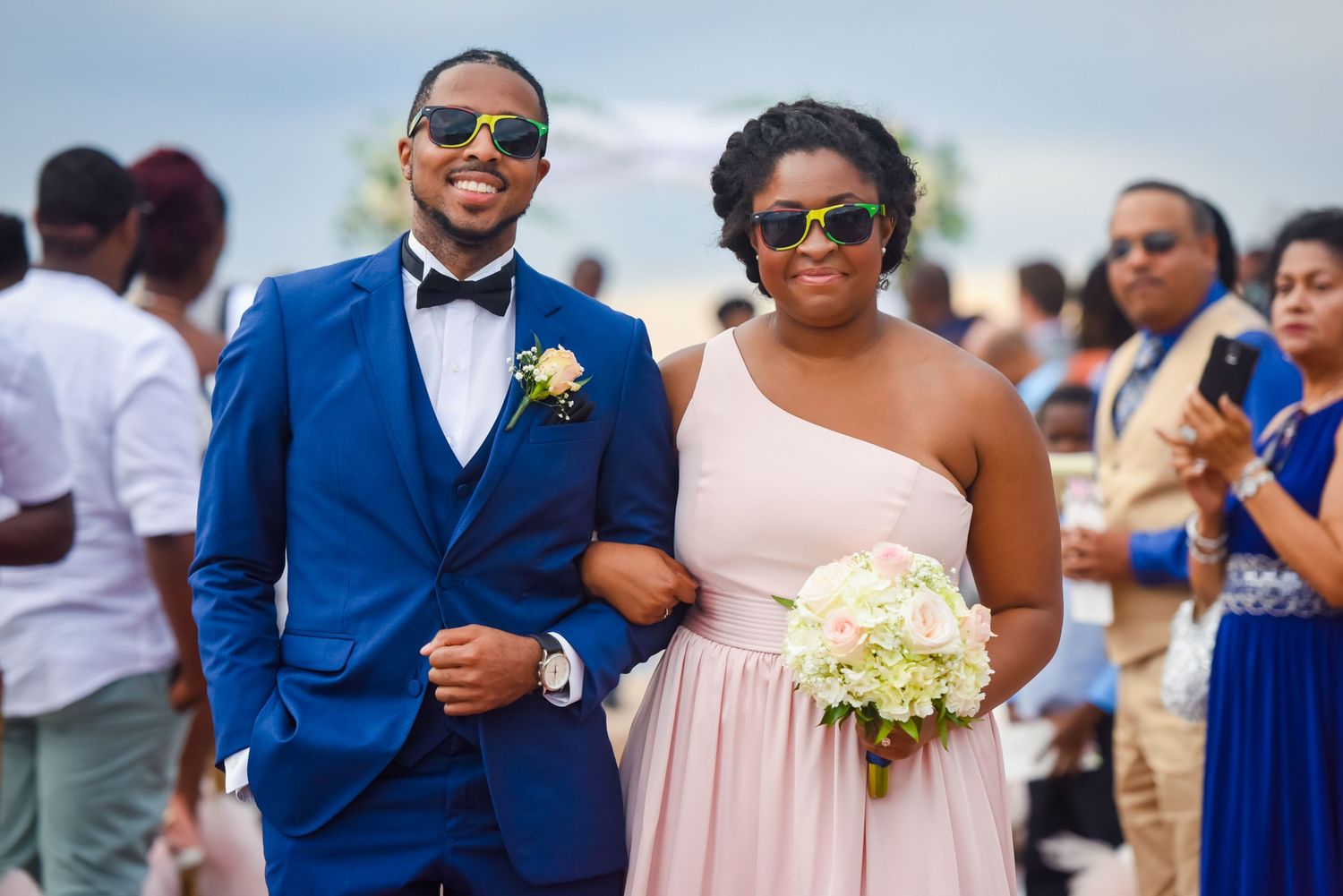 Wedding guests in coordinated blue and pink attire gather at beachside celebration.