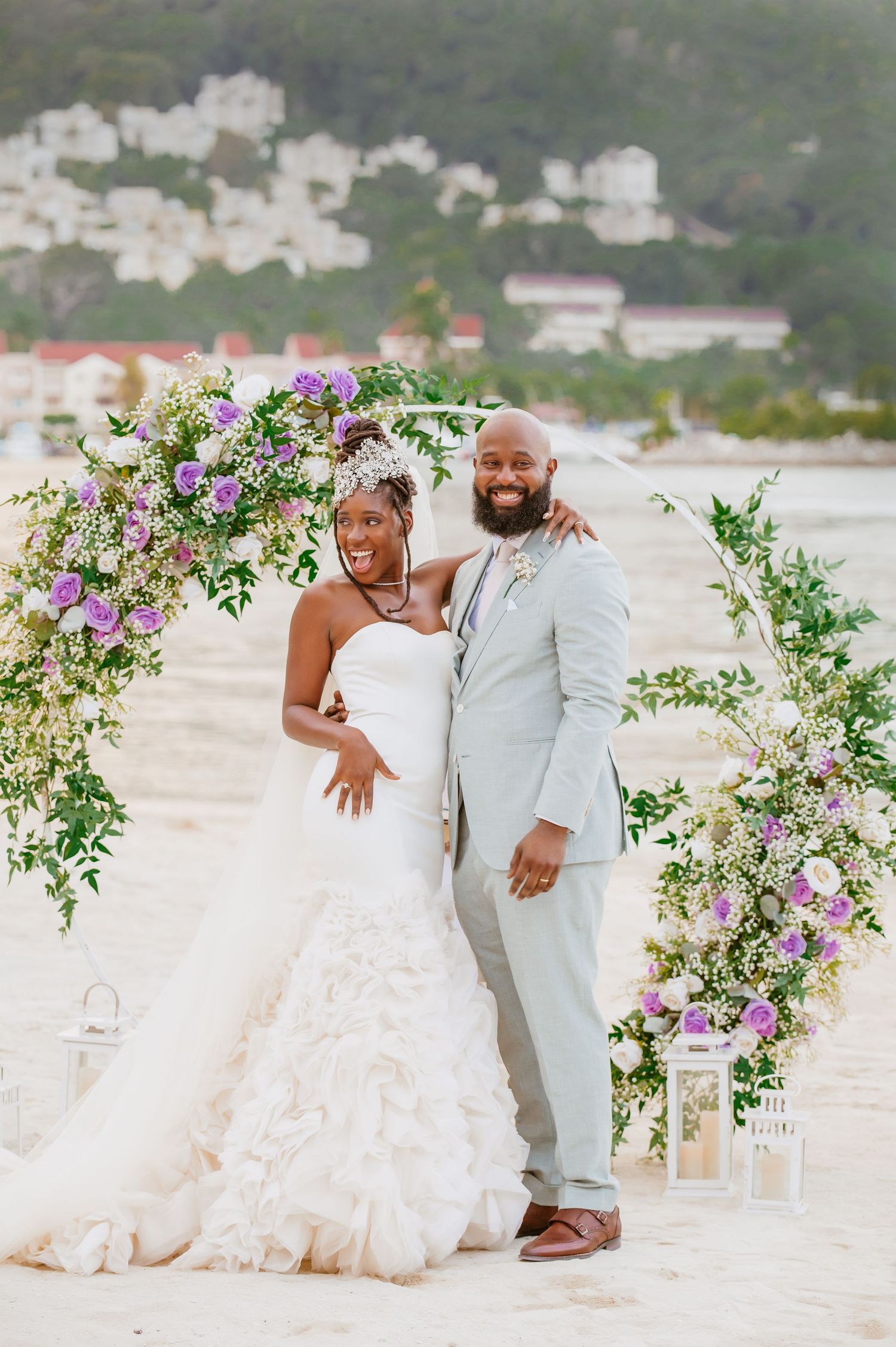 Joyful wedding moment captured on a beach with decorative floral arch and white lanterns.