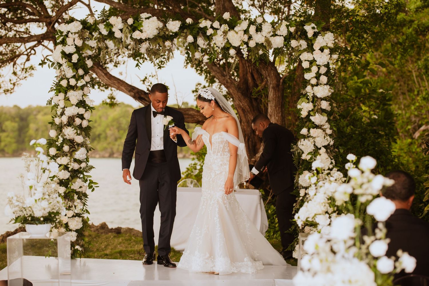 Garden wedding ceremony site decorated with white floral arch and natural foliage.