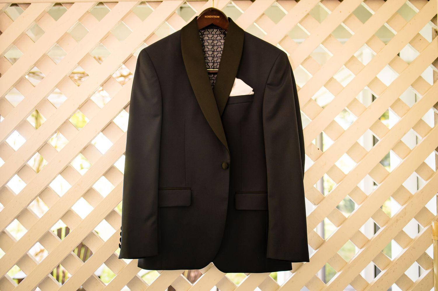 Black suit jackets hang against a lattice backdrop for wedding photography.