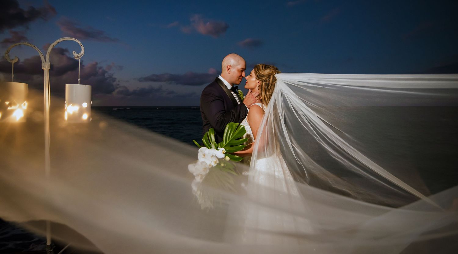 Elegant wedding photo with bride's veil flowing in evening breeze.