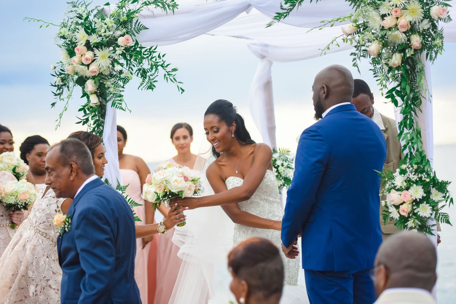 Wedding party stands beneath elegant floral arch during outdoor ceremony with white draping.