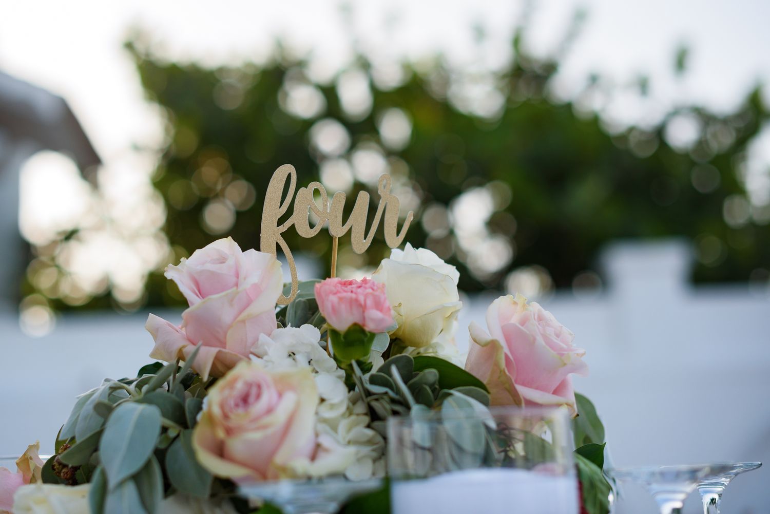 Elegant floral centerpieces with pink roses and greenery decorate outdoor wedding tables.