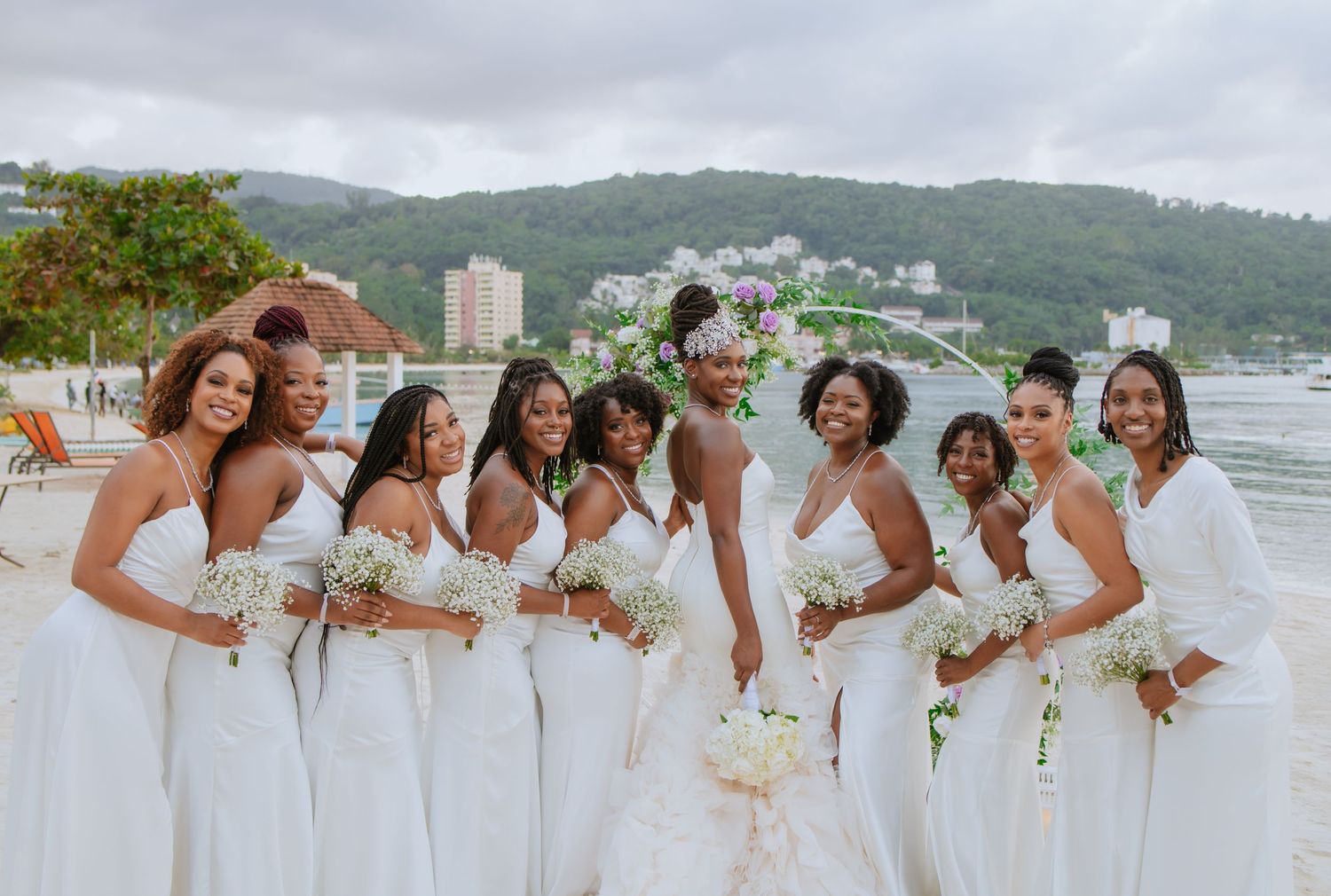 Wedding party in white dresses posing together on a scenic beach.