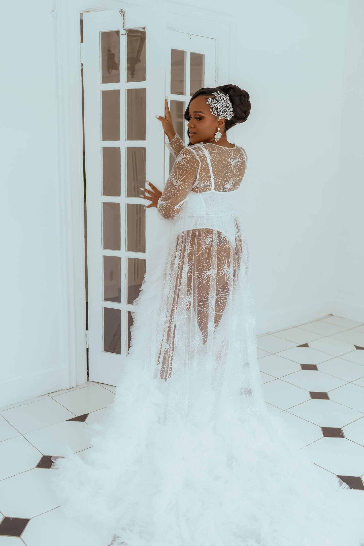 Flowing white wedding dress with long train photographed from behind in a bright interior setting.