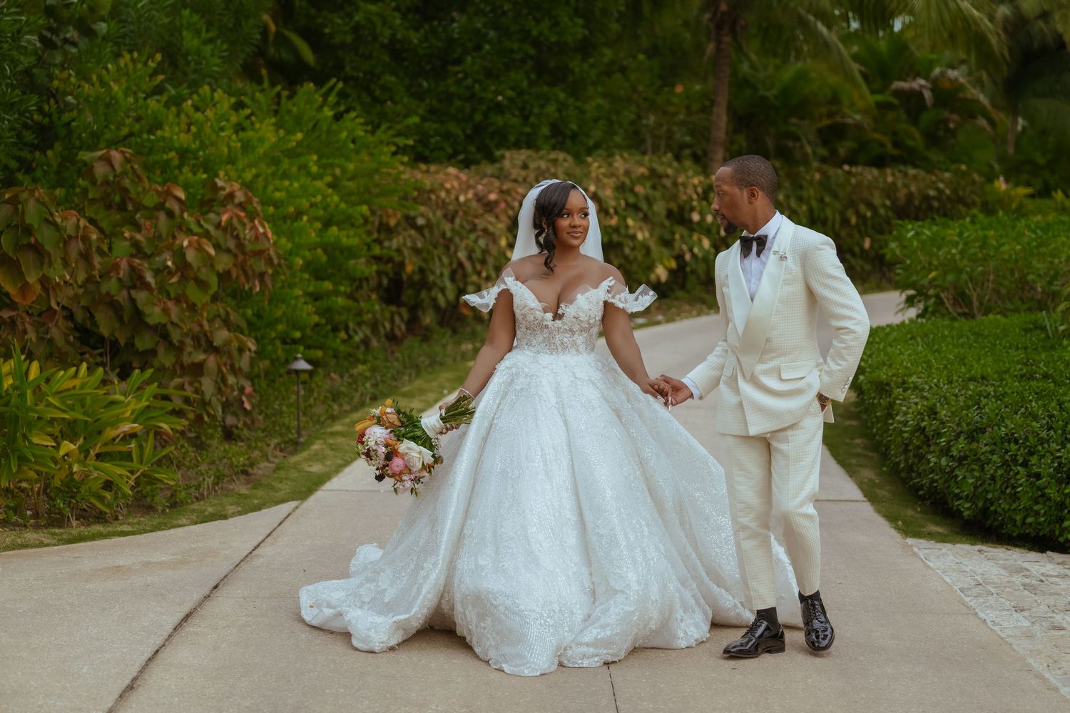 Wedding couple posing for romantic photos on garden pathway surrounded by greenery.