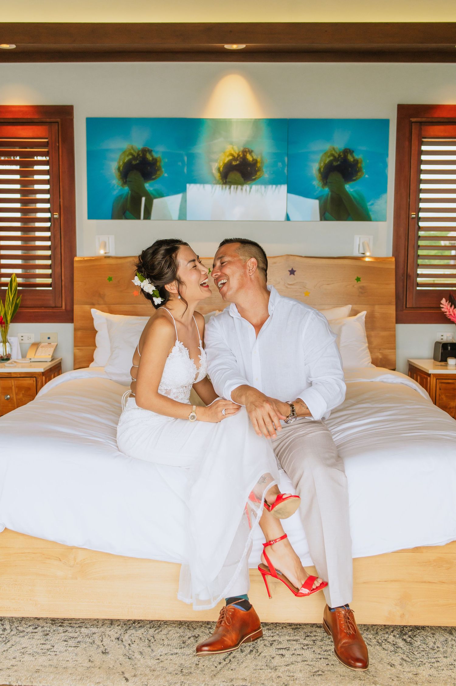 Two people in white clothing relax together on a white bed with wooden accents.