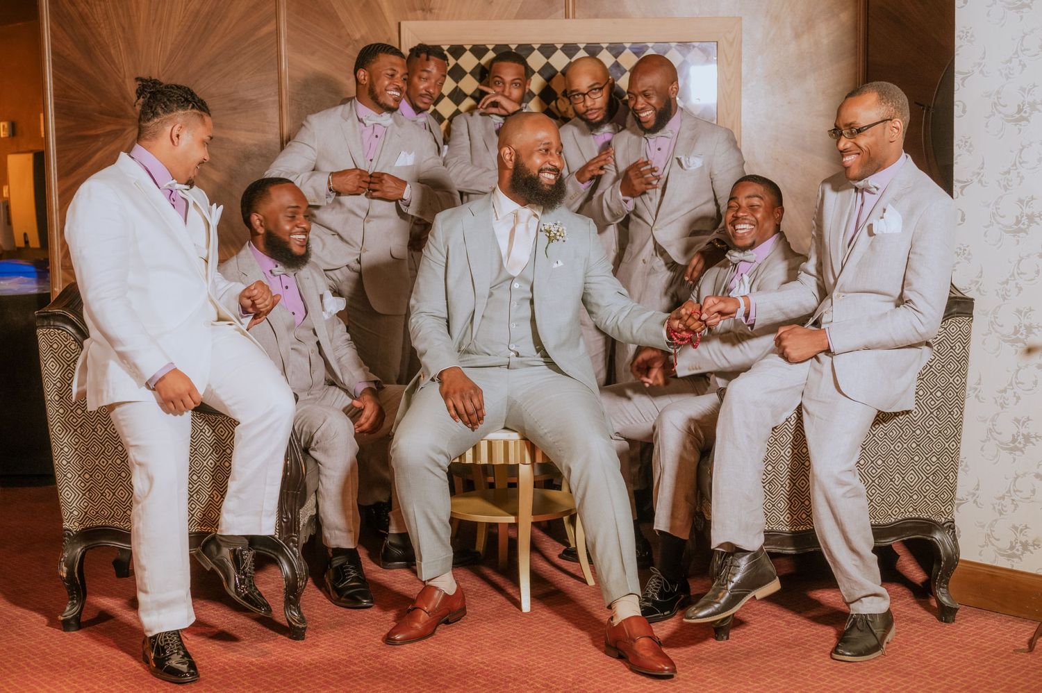 Wedding party in coordinated light gray suits sitting together and sharing laughs.