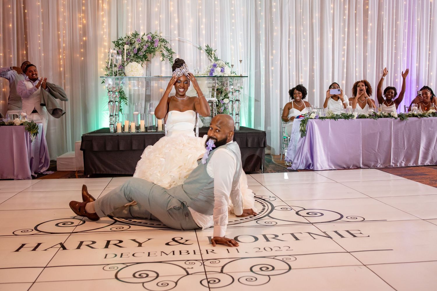 A couple performs a traditional wedding garter removal ritual on an elegant dance floor with decorative patterns.