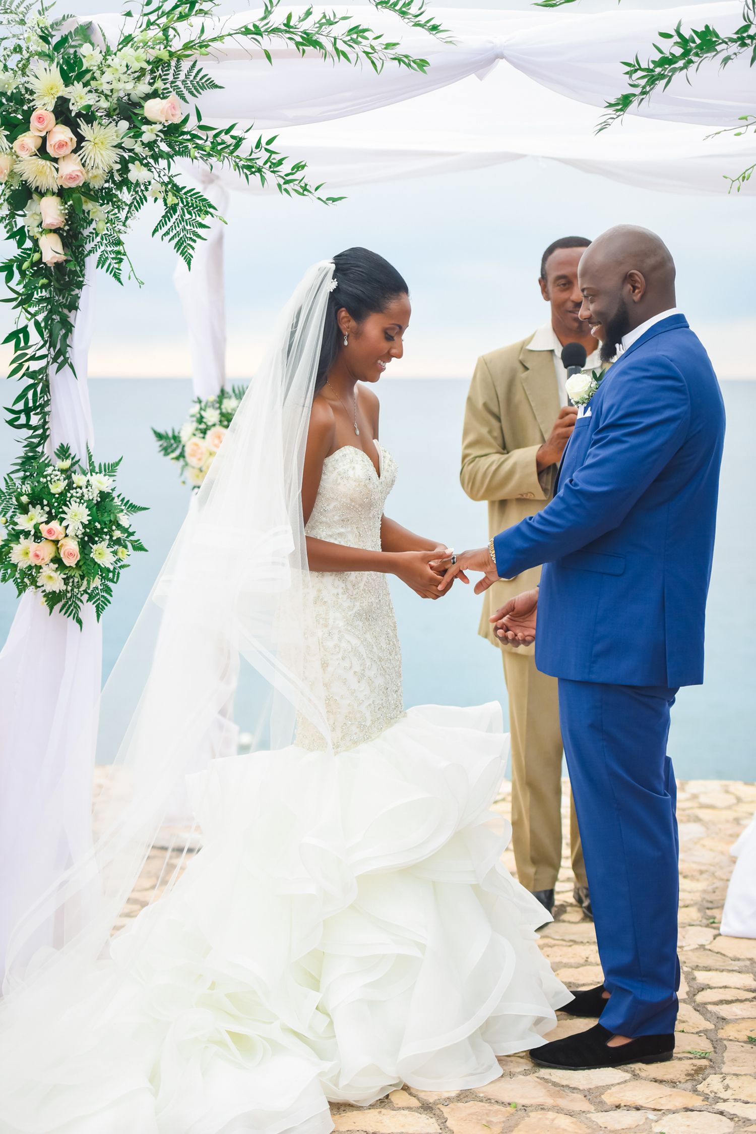 Seaside wedding ceremony with white draping and floral arrangements against ocean backdrop.