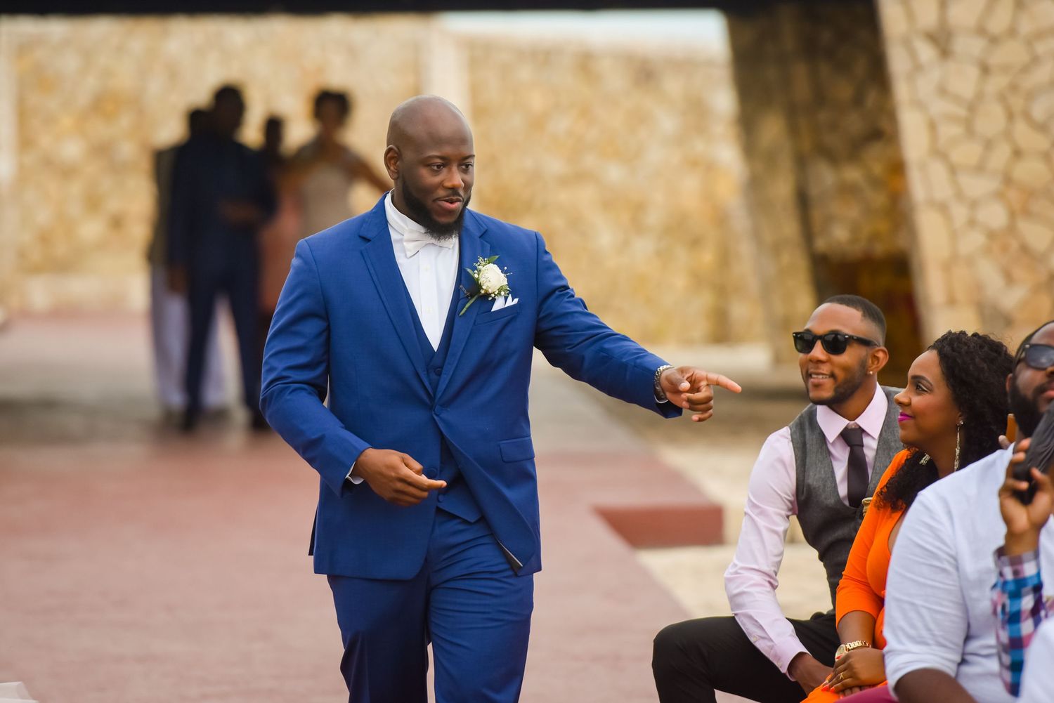 Wedding attendee in royal blue suit interacting with seated guests at outdoor venue.