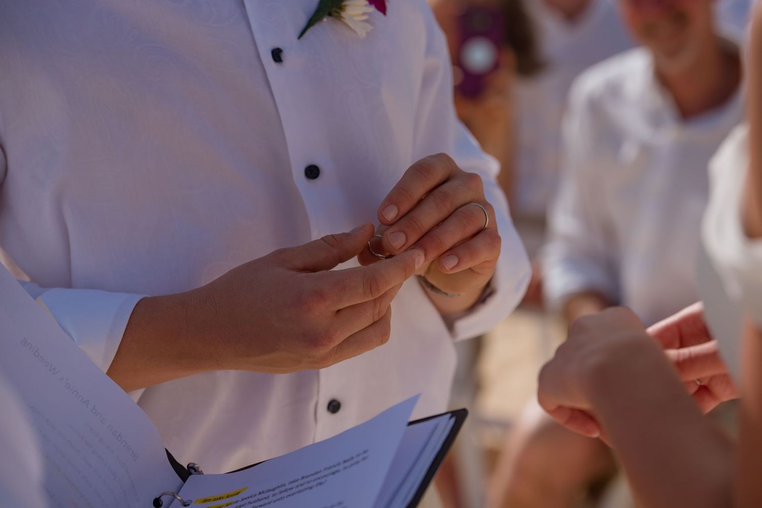 Close-up of hands during ring exchange at beach wedding ceremony.