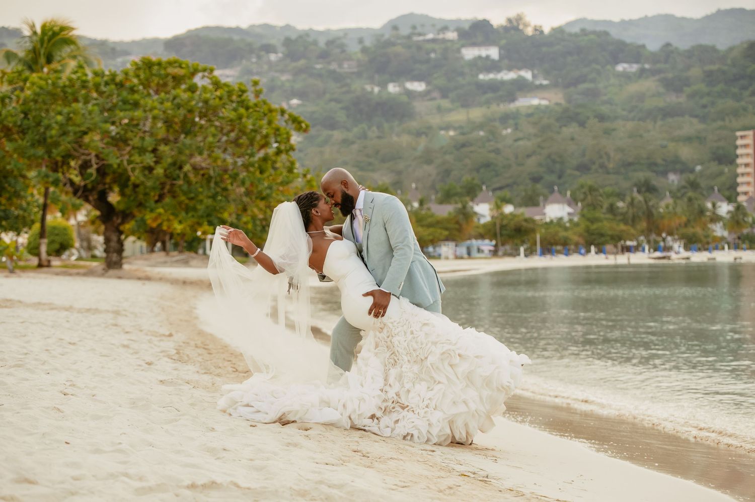 A romantic beach wedding portrait with flowing veil and coastal scenery.