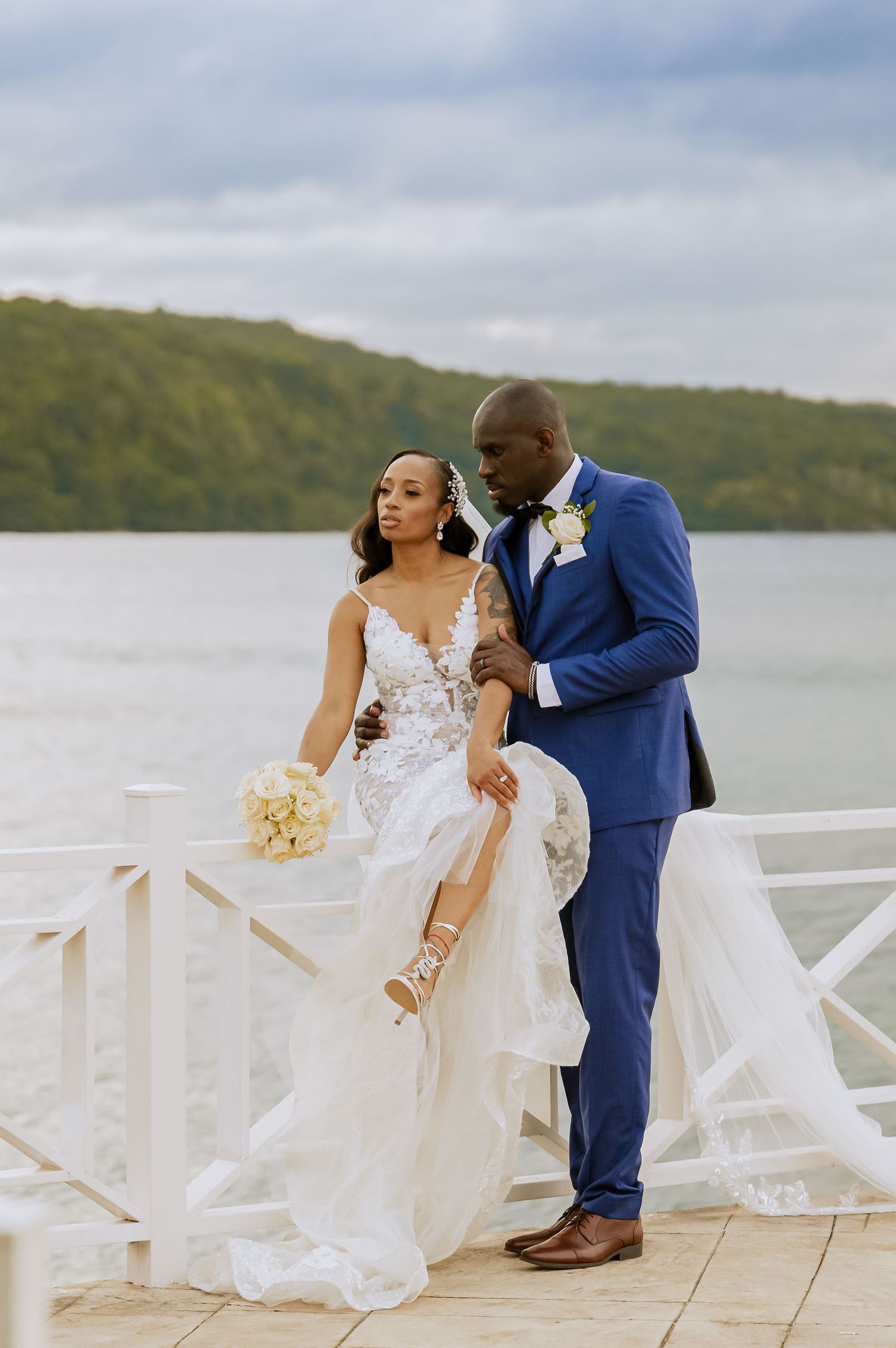 Newlyweds share romantic moment on white deck overlooking scenic bay and hills.