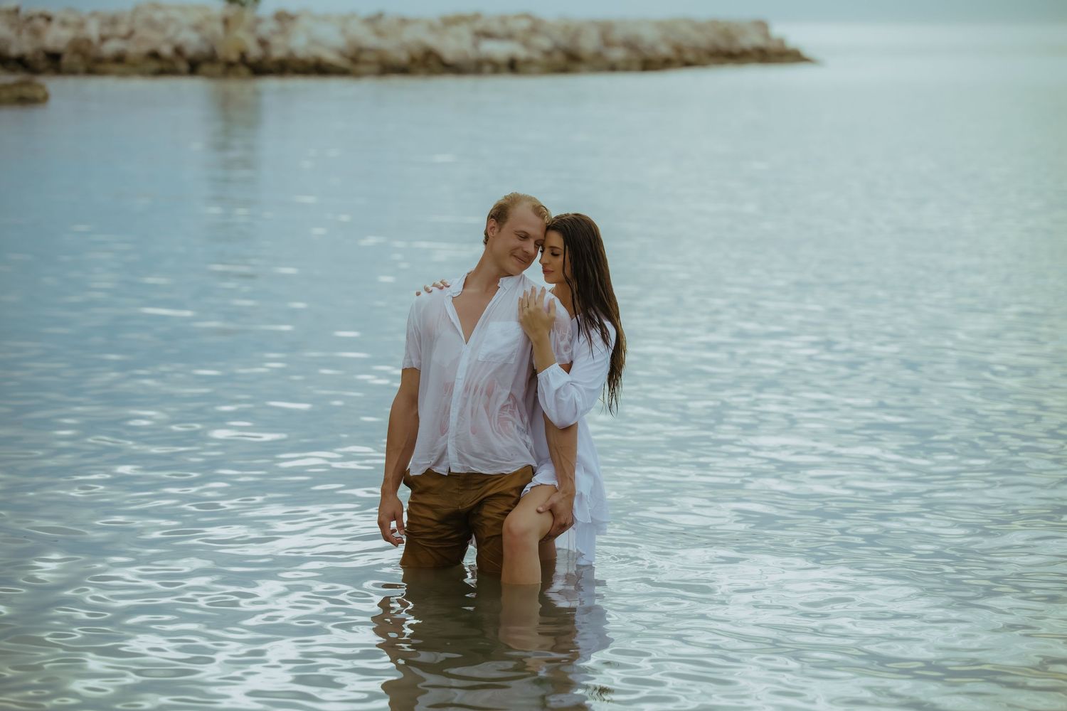 A couple shares an intimate moment while standing in crystal clear ocean waters.