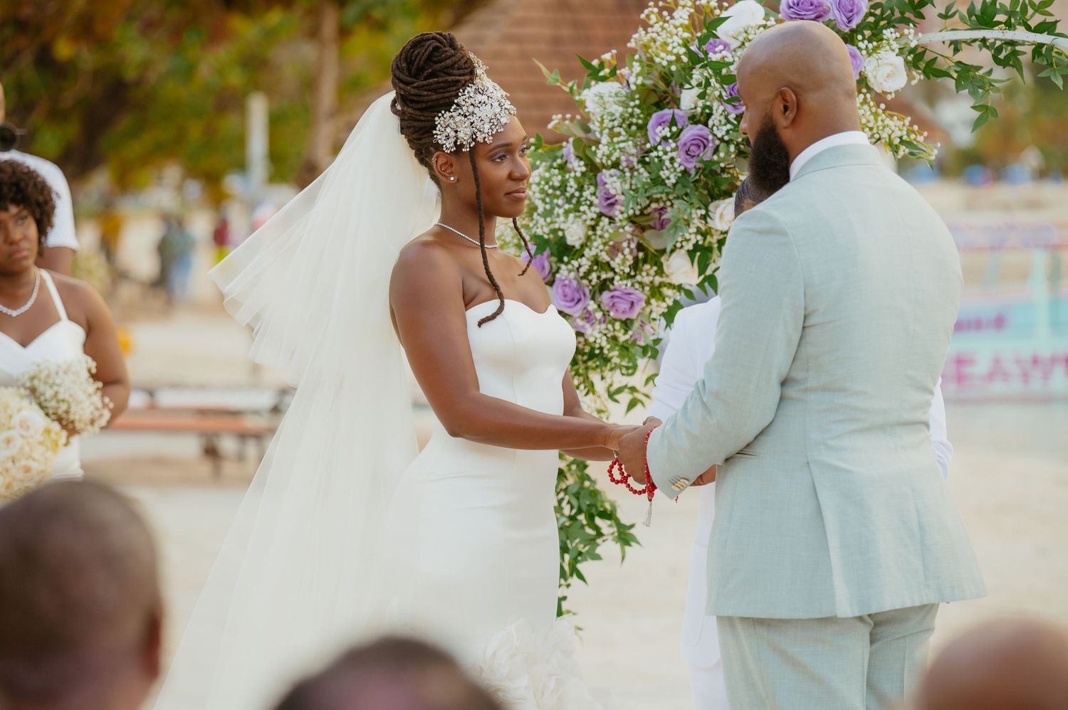 Elegant beach wedding ceremony with floral arrangements and guests in white attire.