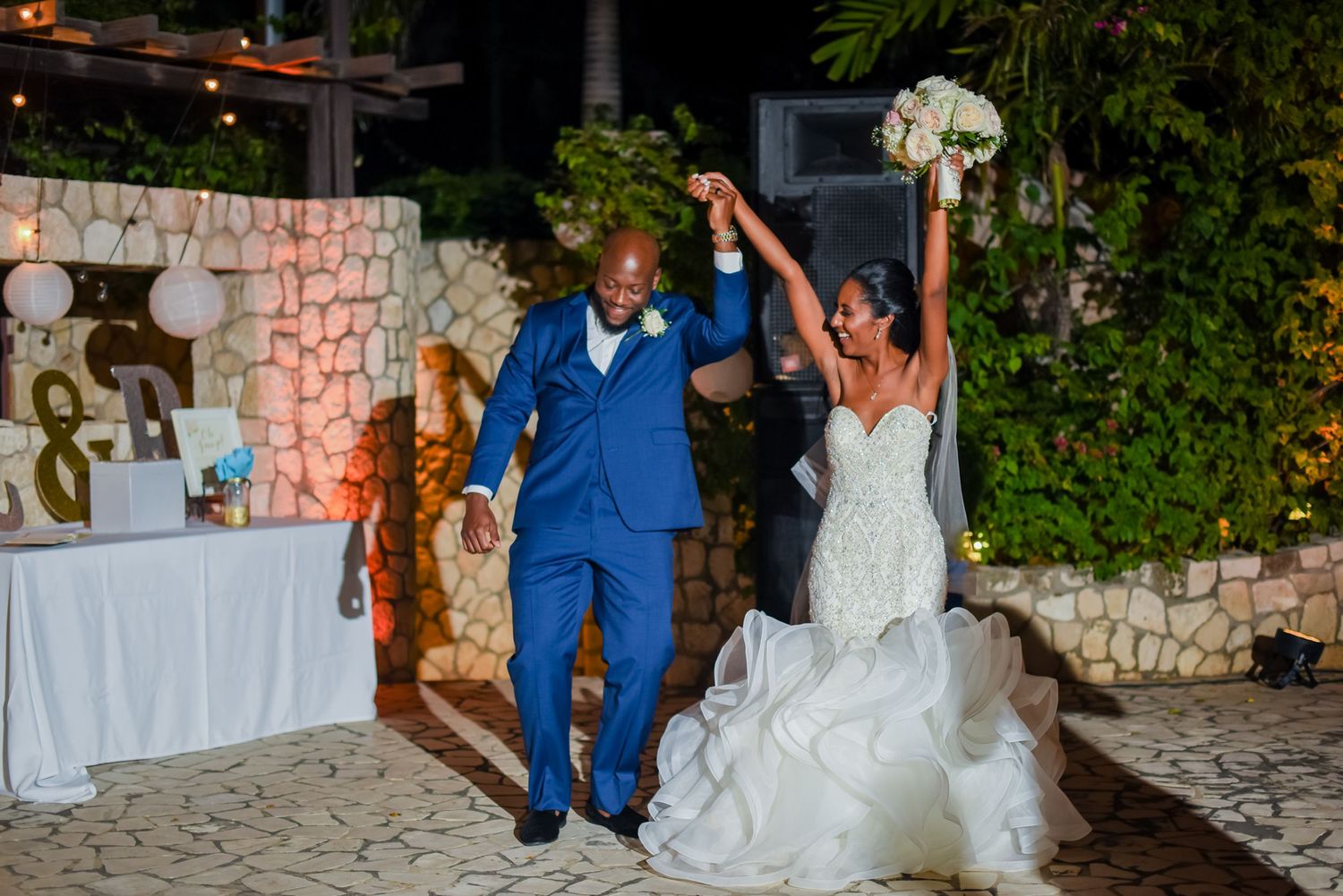 Wedding celebration on a stone patio with decorative lighting and white table settings.