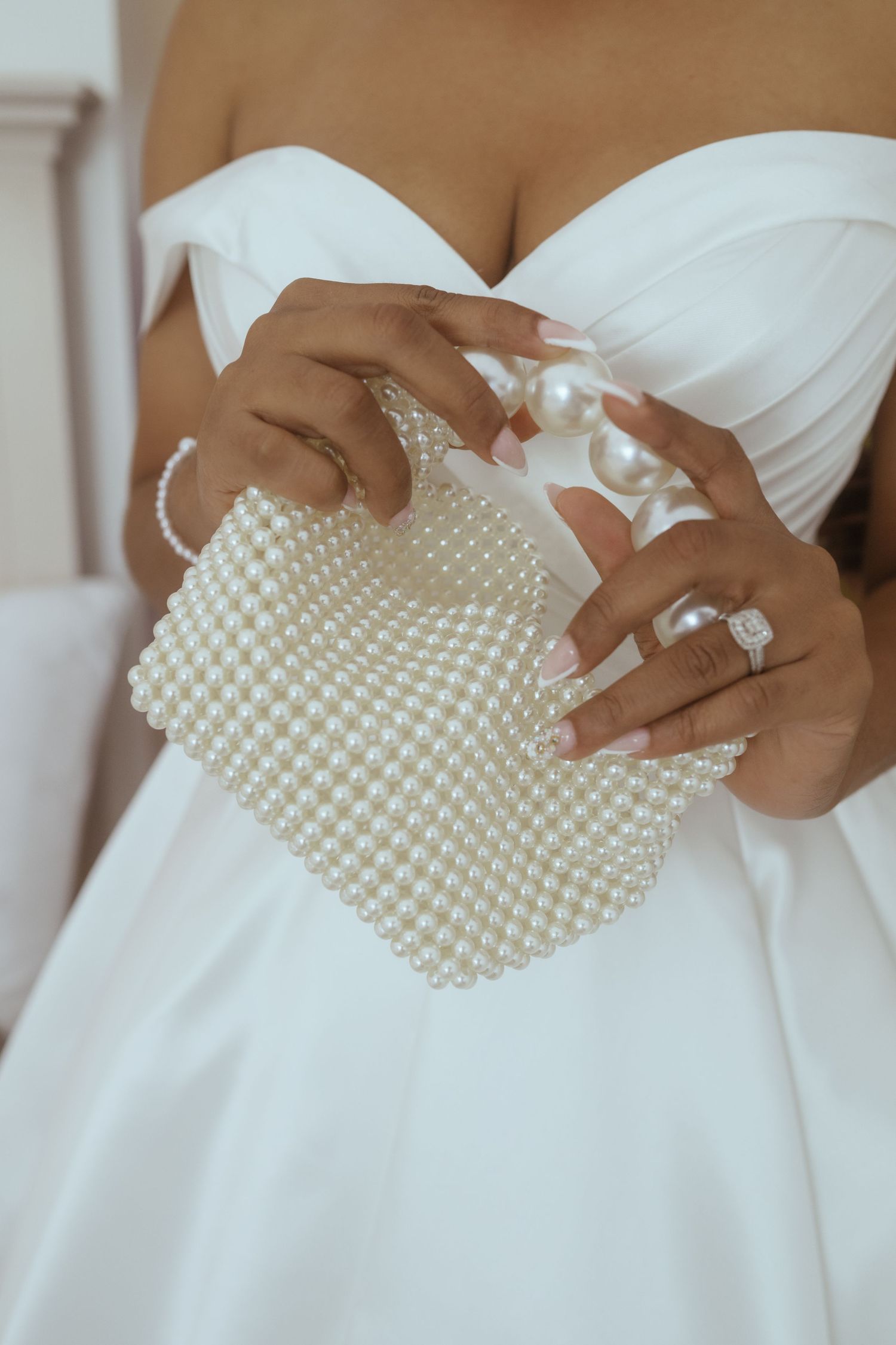 Close-up of bride's white dress with pearl embellished details and delicate hand placement.