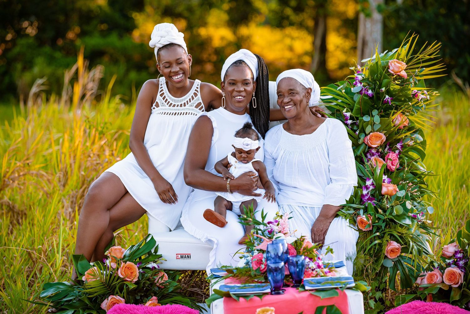 Three generations gather for an elegant outdoor tea party with floral decorations in a sunlit meadow.