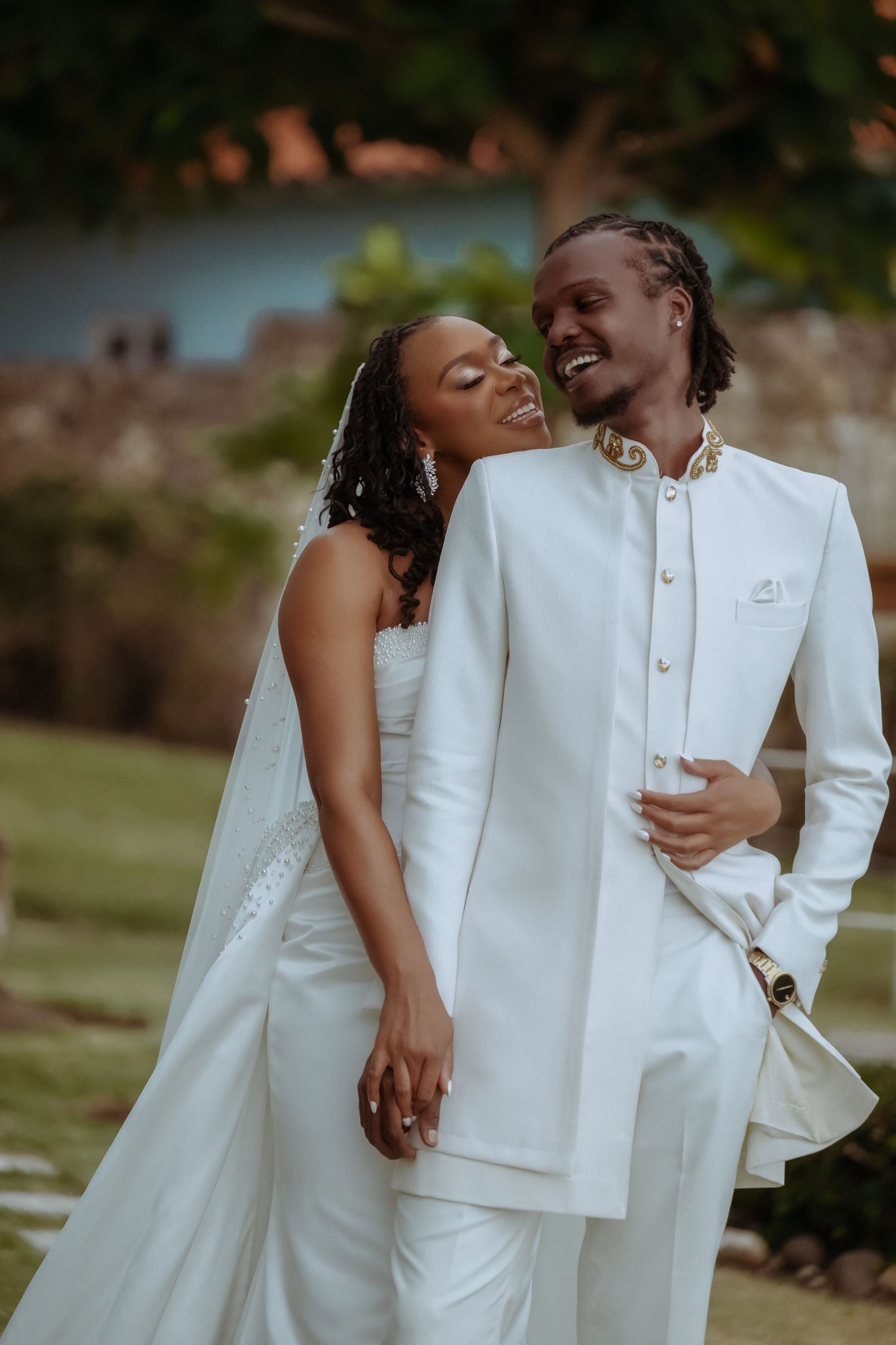 A joyful wedding couple in all-white attire sharing a tender moment outdoors.