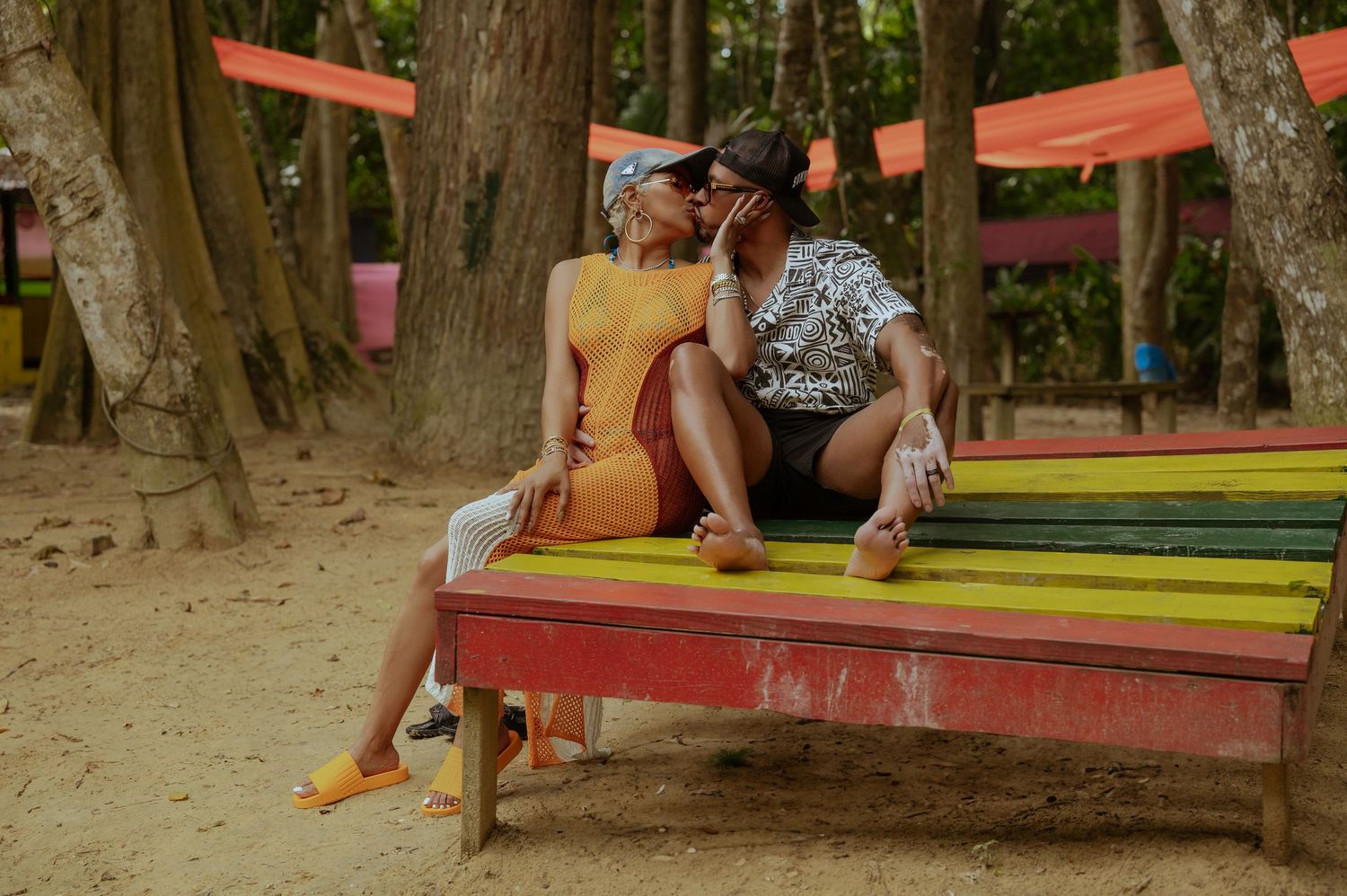 Couple enjoying a romantic picnic by a lake with red and yellow blankets spread out on the ground.