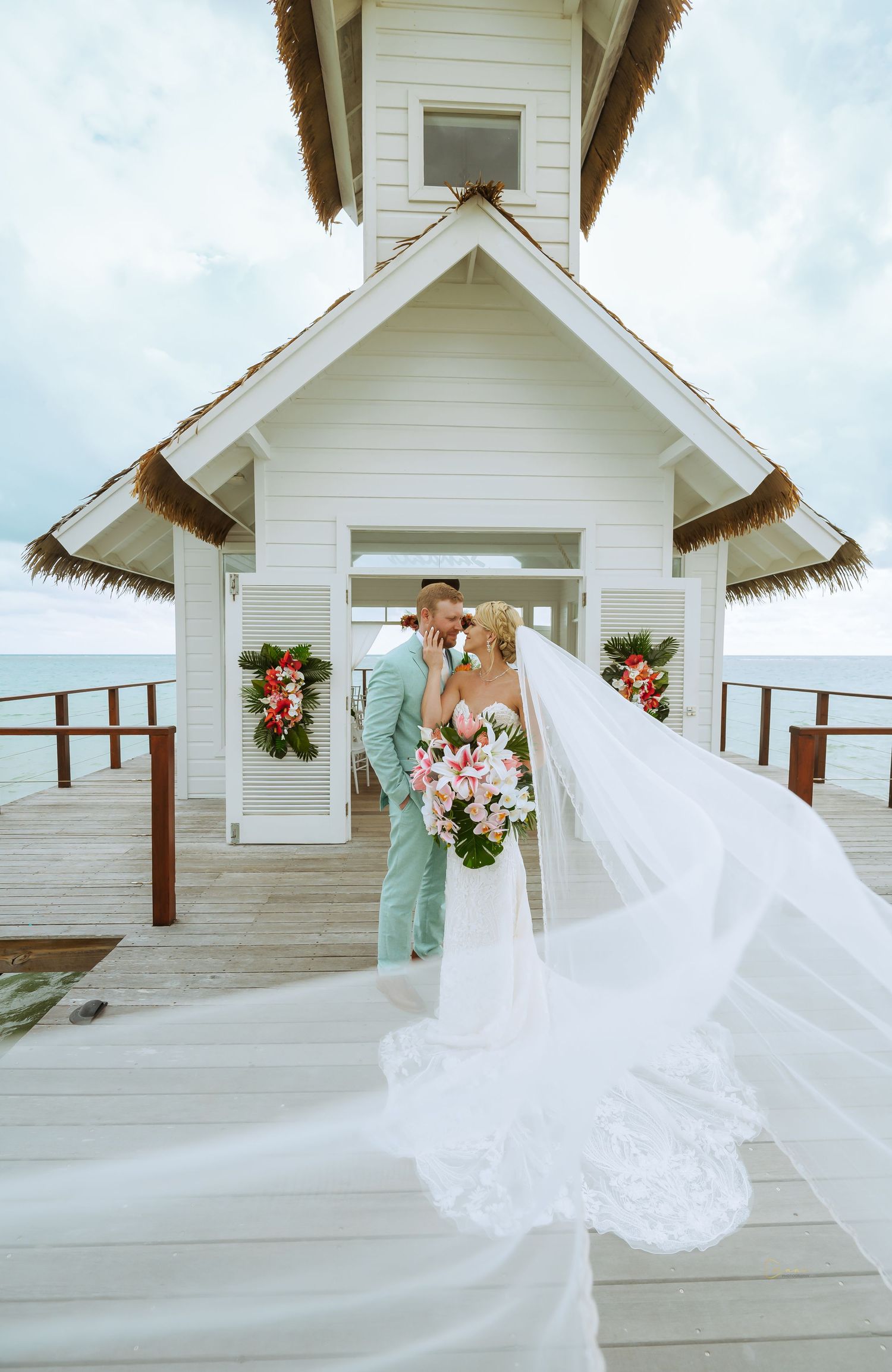 A romantic wedding ceremony on an overwater chapel with white decor and floral arrangements by the ocean.