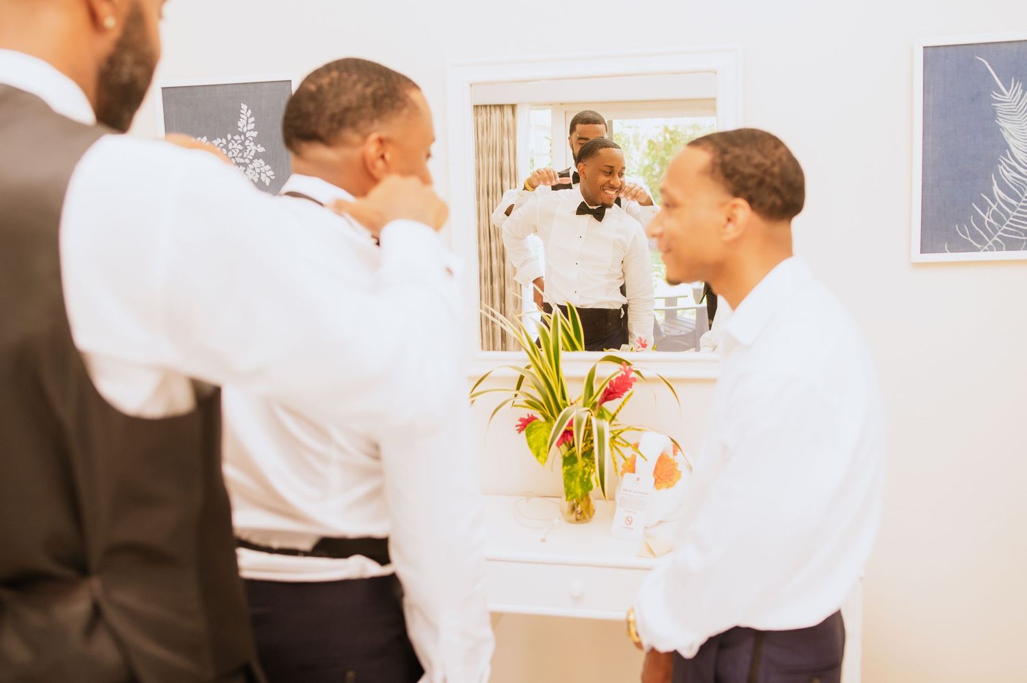 Groomsmen interact during pre-wedding preparations in a bright indoor space.