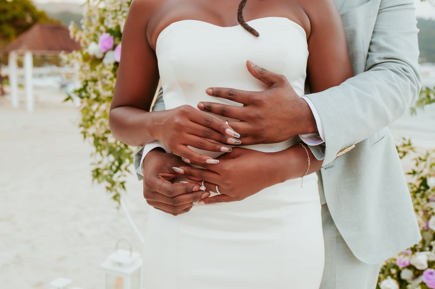 Romantic beach wedding couple embraces during golden hour with mountains and ocean in background.