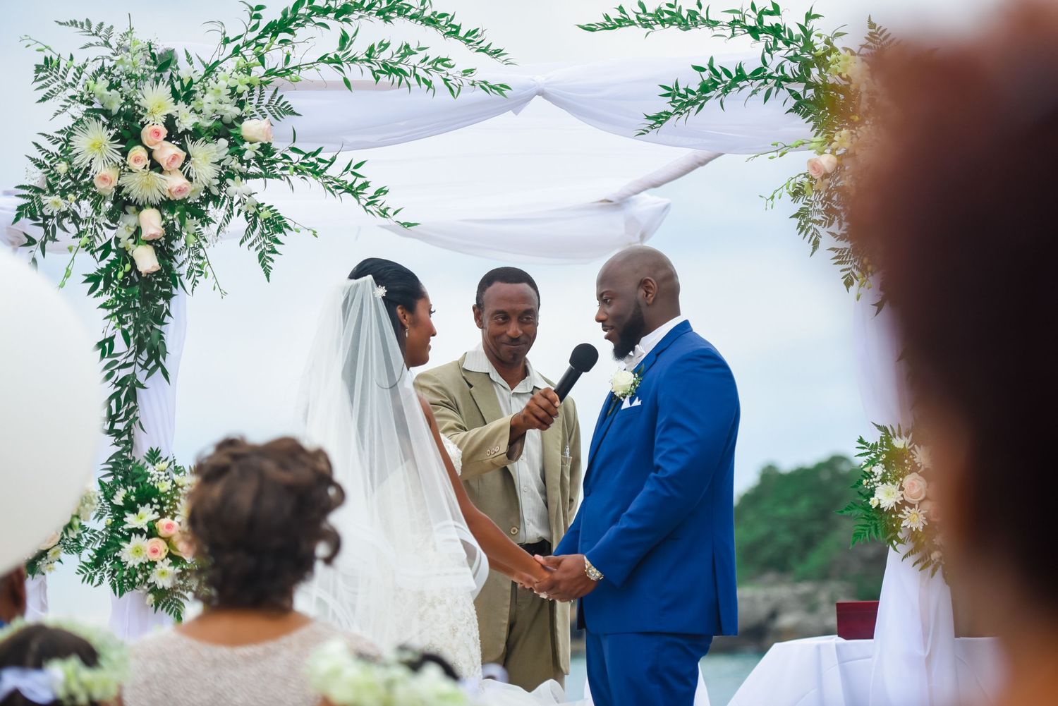 Wedding officiant conducts ceremony under decorative arch with flowers and greenery.
