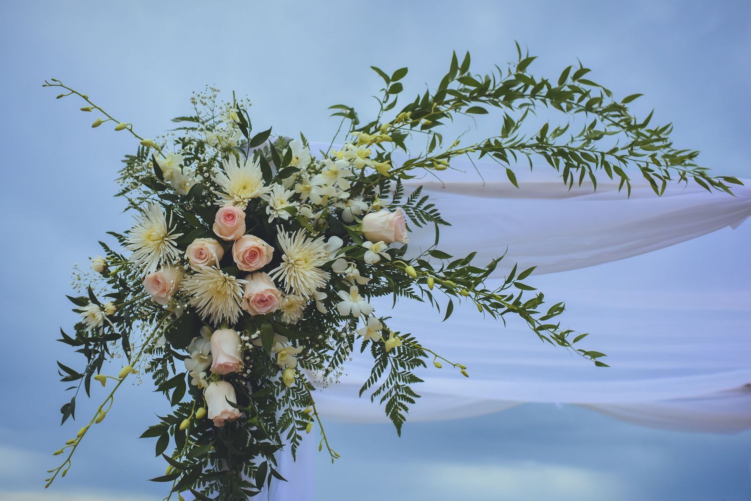 Beautiful floral arrangements with pink roses and greenery decorating a seaside wedding venue.