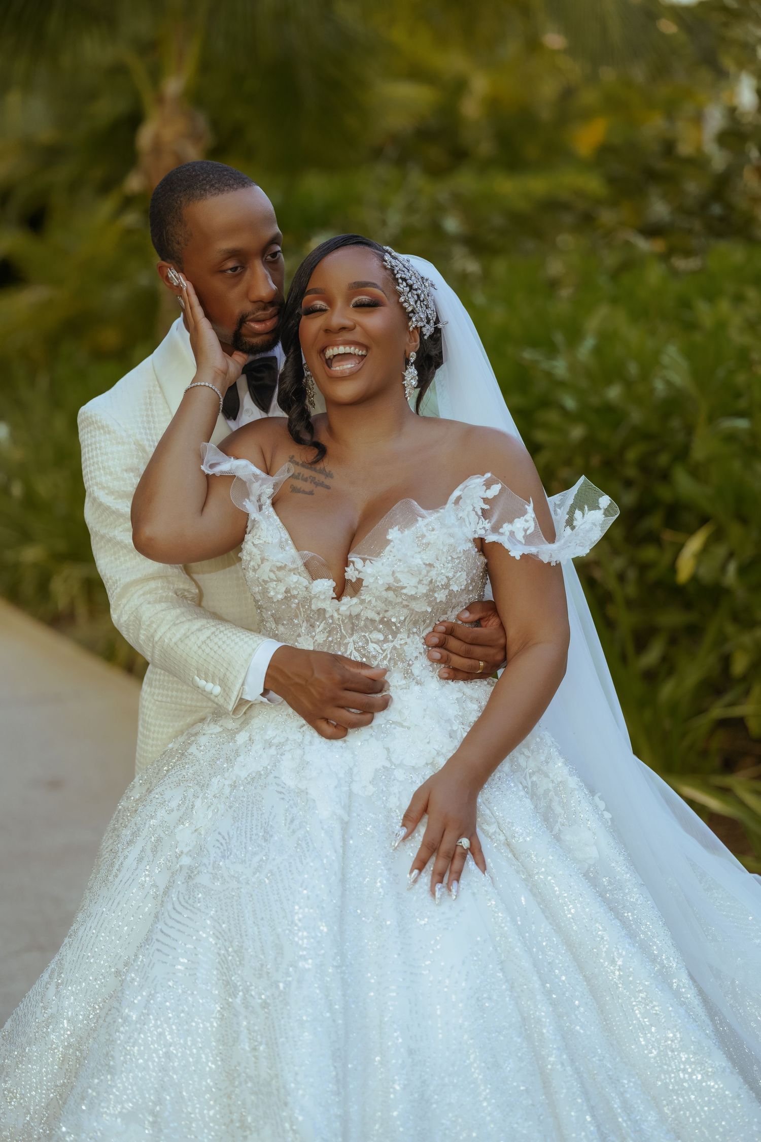 Romantic wedding couple embracing outdoors in formal attire against natural backdrop.
