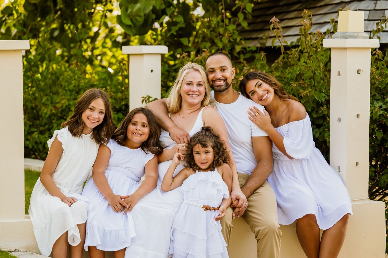 Family wearing coordinated white outfits poses together for a summer portrait outdoors.