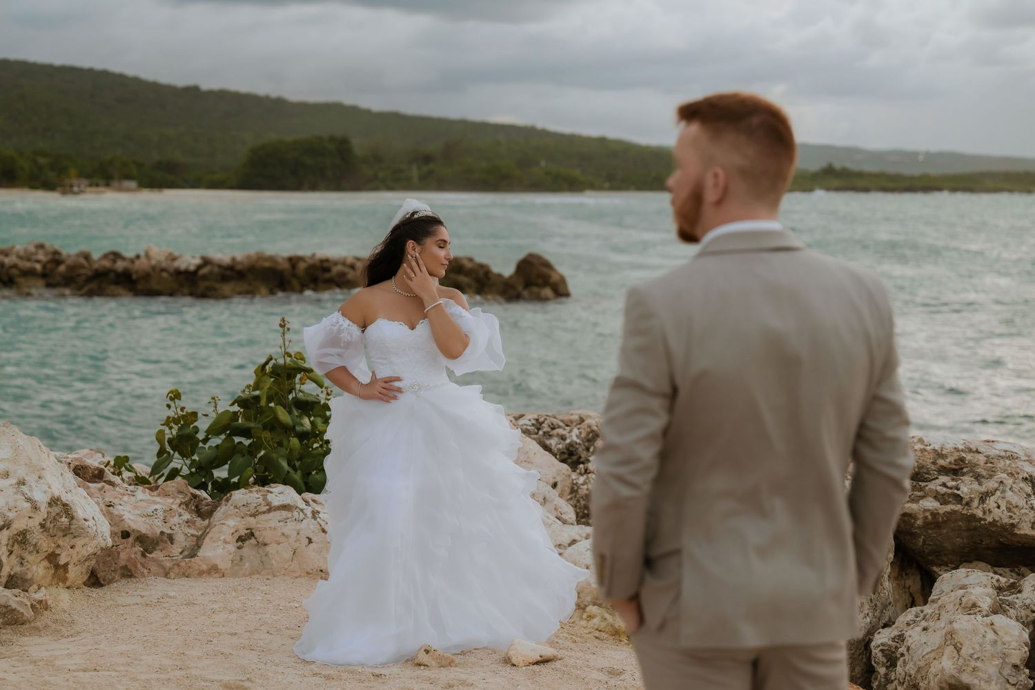 Couple in wedding attire standing together on rocky coastal shoreline.