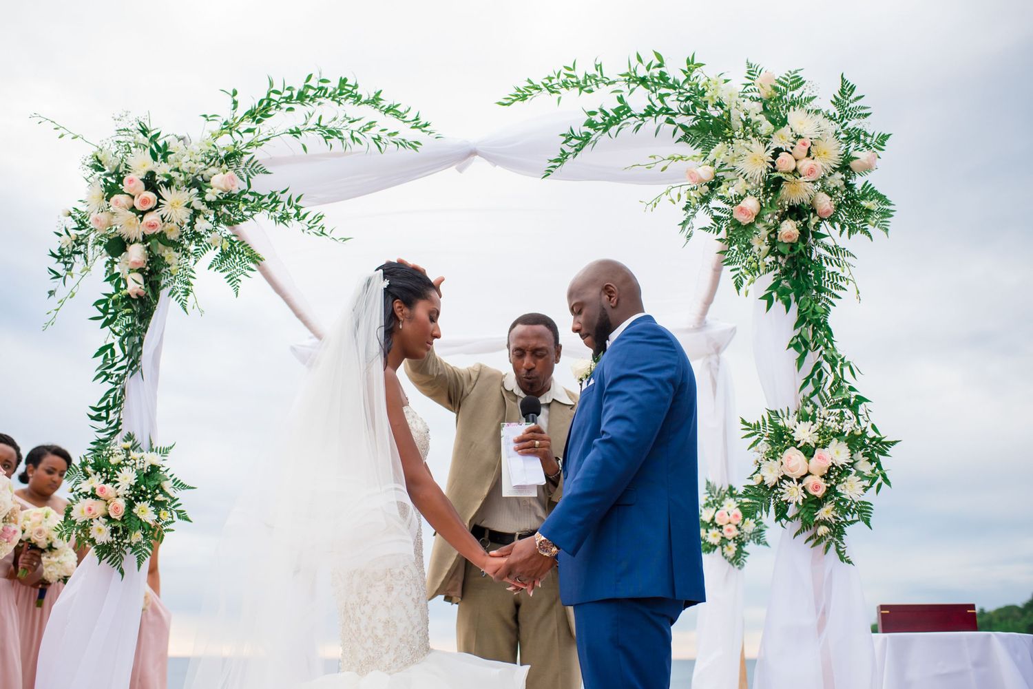 Outdoor wedding ceremony with romantic floral arch and white fabric draping.