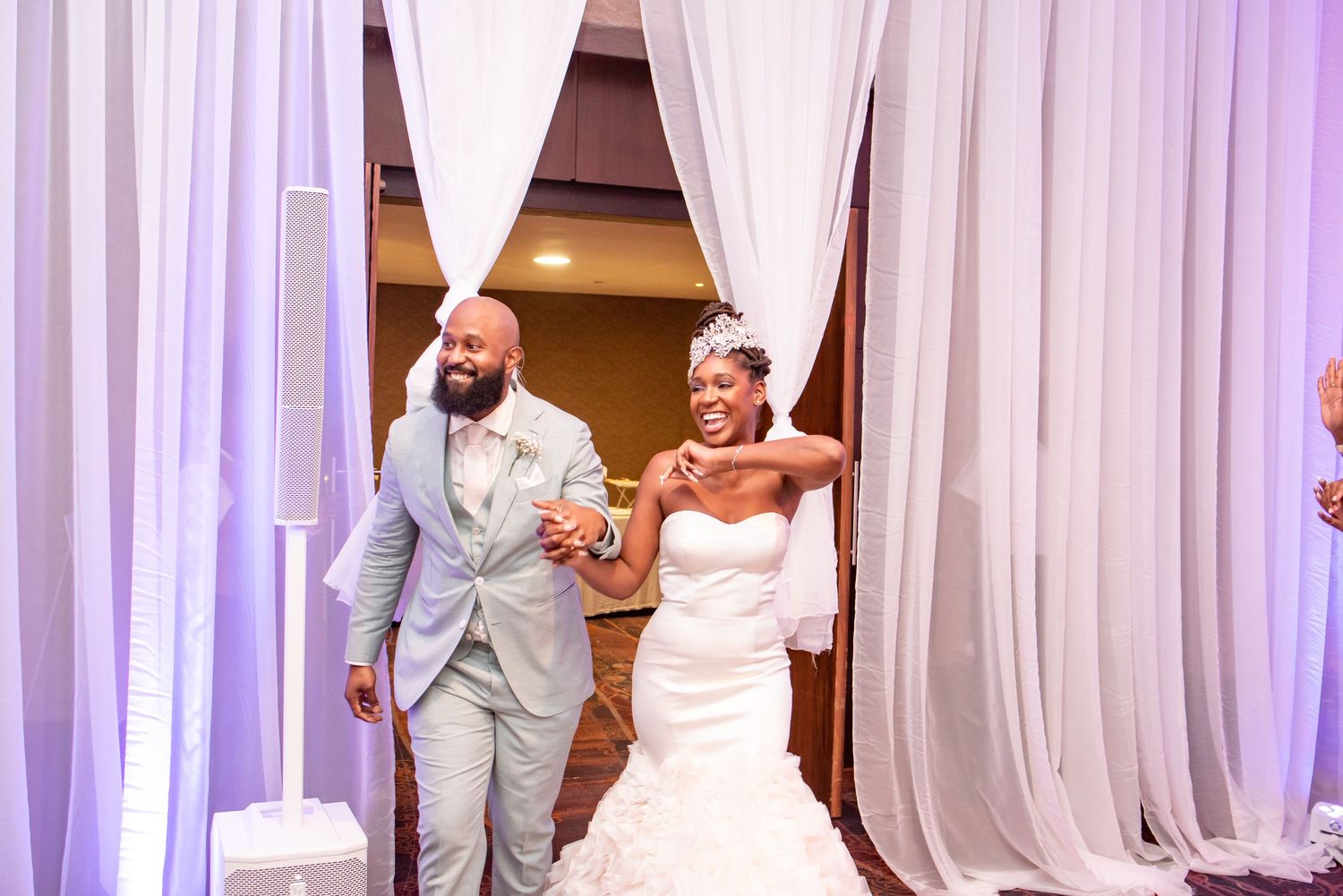 A couple makes their grand entrance through white curtains at their wedding reception.