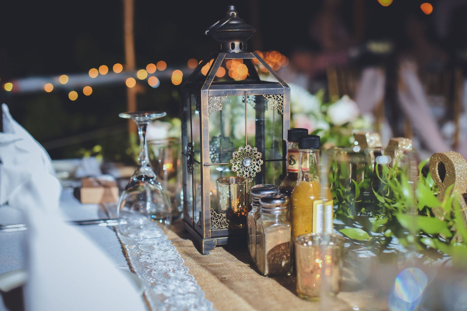 Wedding reception table setup with glowing lanterns and elegant glassware at dusk.
