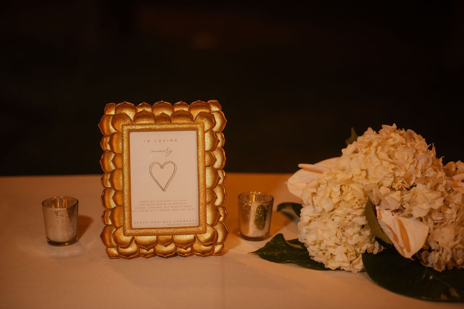 Gold framed heart artwork displayed with white flowers and candles on reception table.