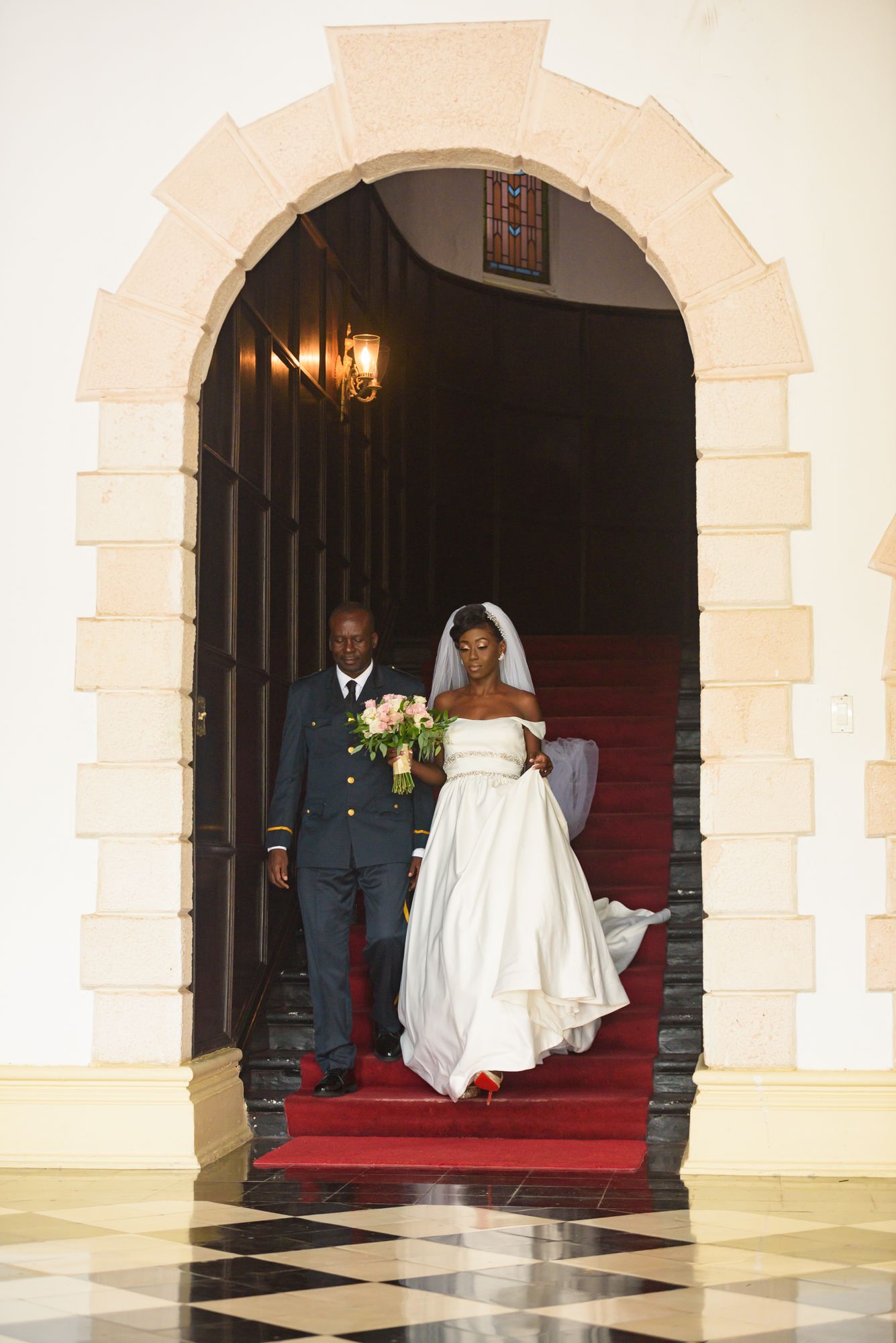 Wedding ceremony entrance through stone archways with red carpet and dramatic lighting.