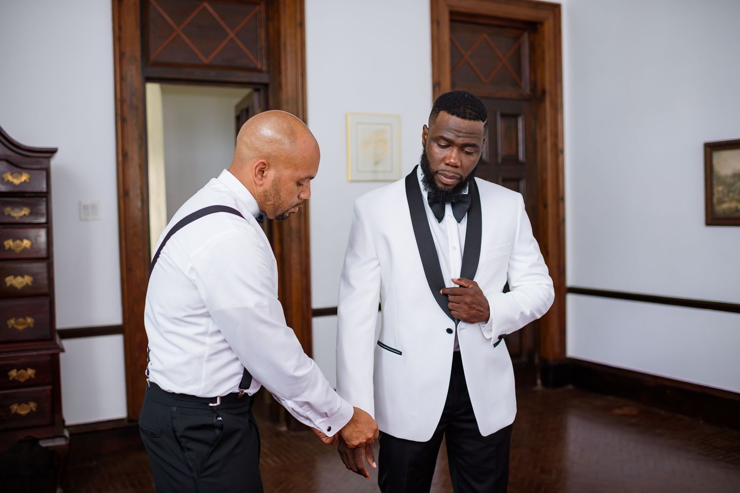 Formal event preparation scene with people in white tuxedo jackets and dark pants.