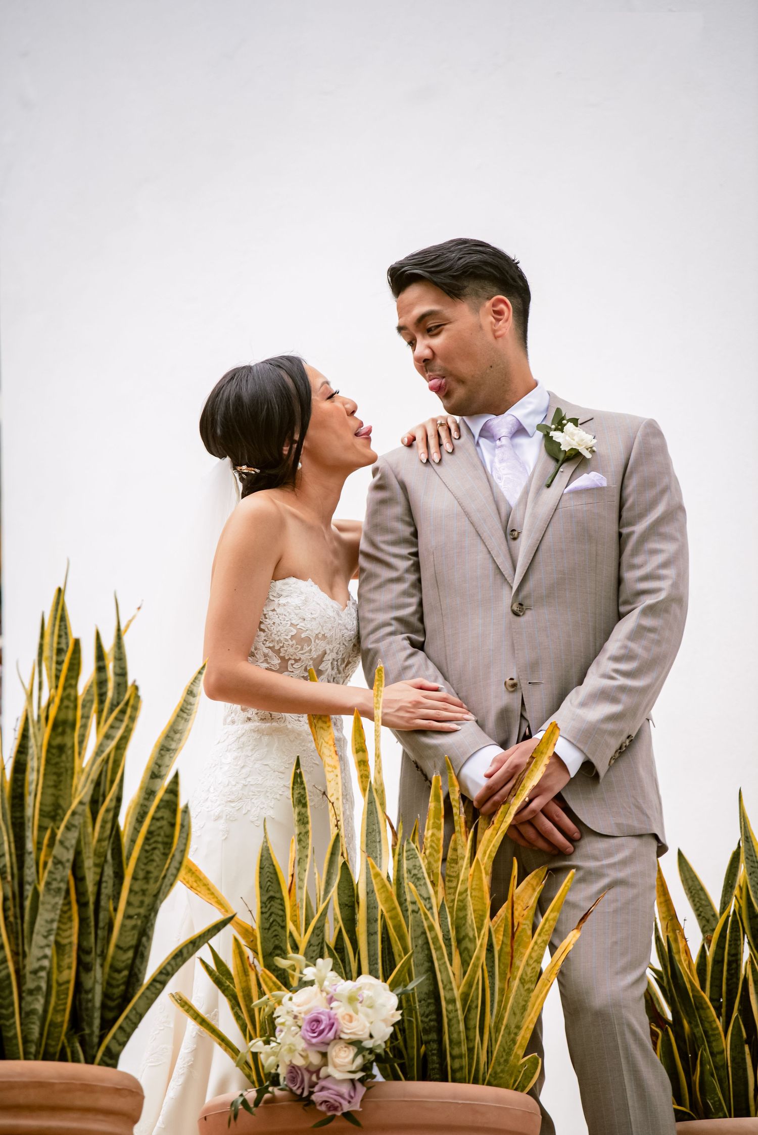 Newlyweds share intimate moments against a backdrop of tall snake plants in elegant wedding attire.