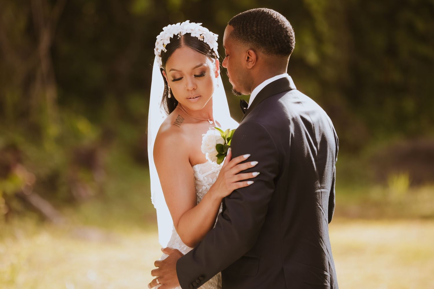 A tender wedding moment captured in warm sunlight against natural foliage.