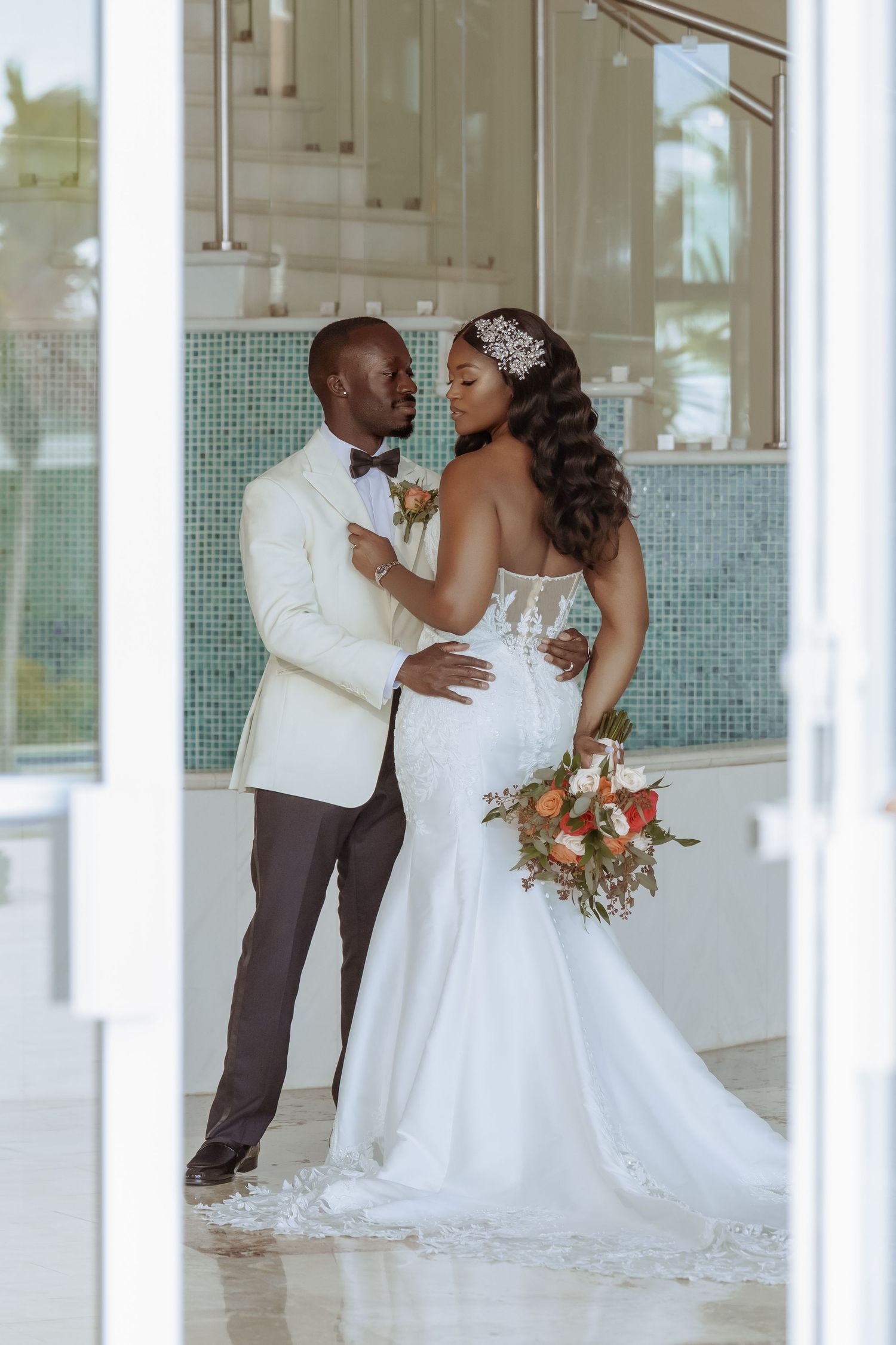 Romantic wedding photoshoot with couple in white attire posing in front of a bright modern interior space.