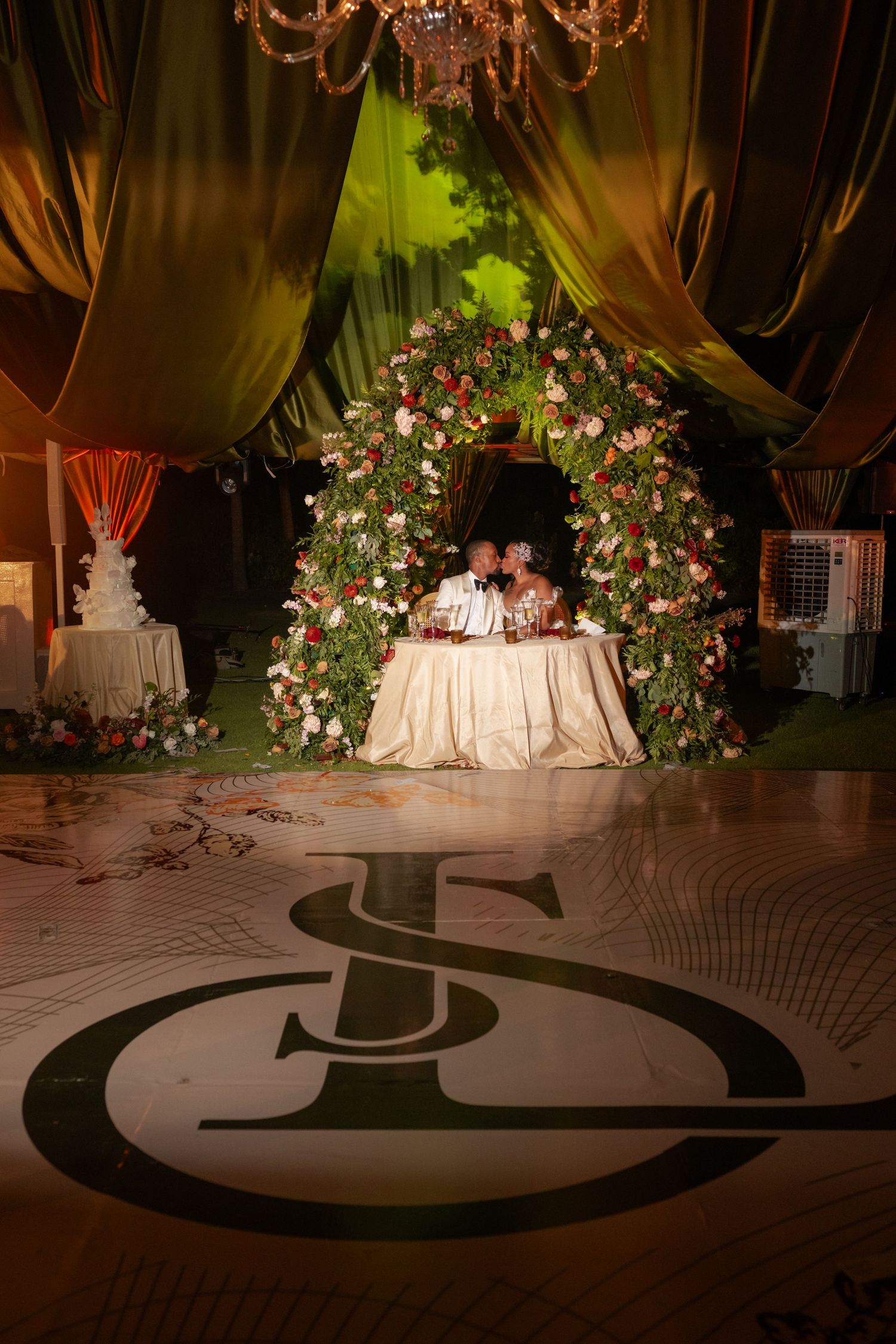 Wedding reception dance floor with custom monogram design and floral decorations under chandeliers.