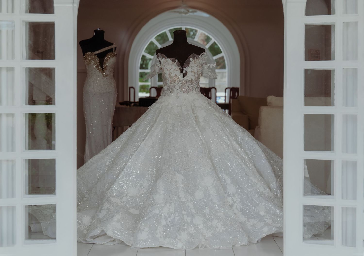 A bride in a voluminous white ball gown poses in front of arched windows in a grand hallway.