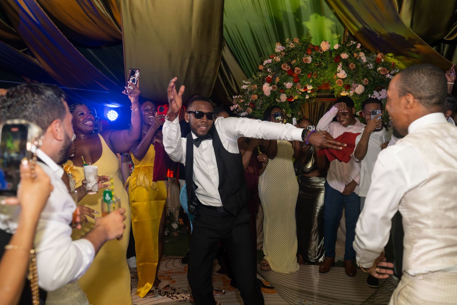 Wedding party dancing and celebrating during evening reception under decorative lighting.
