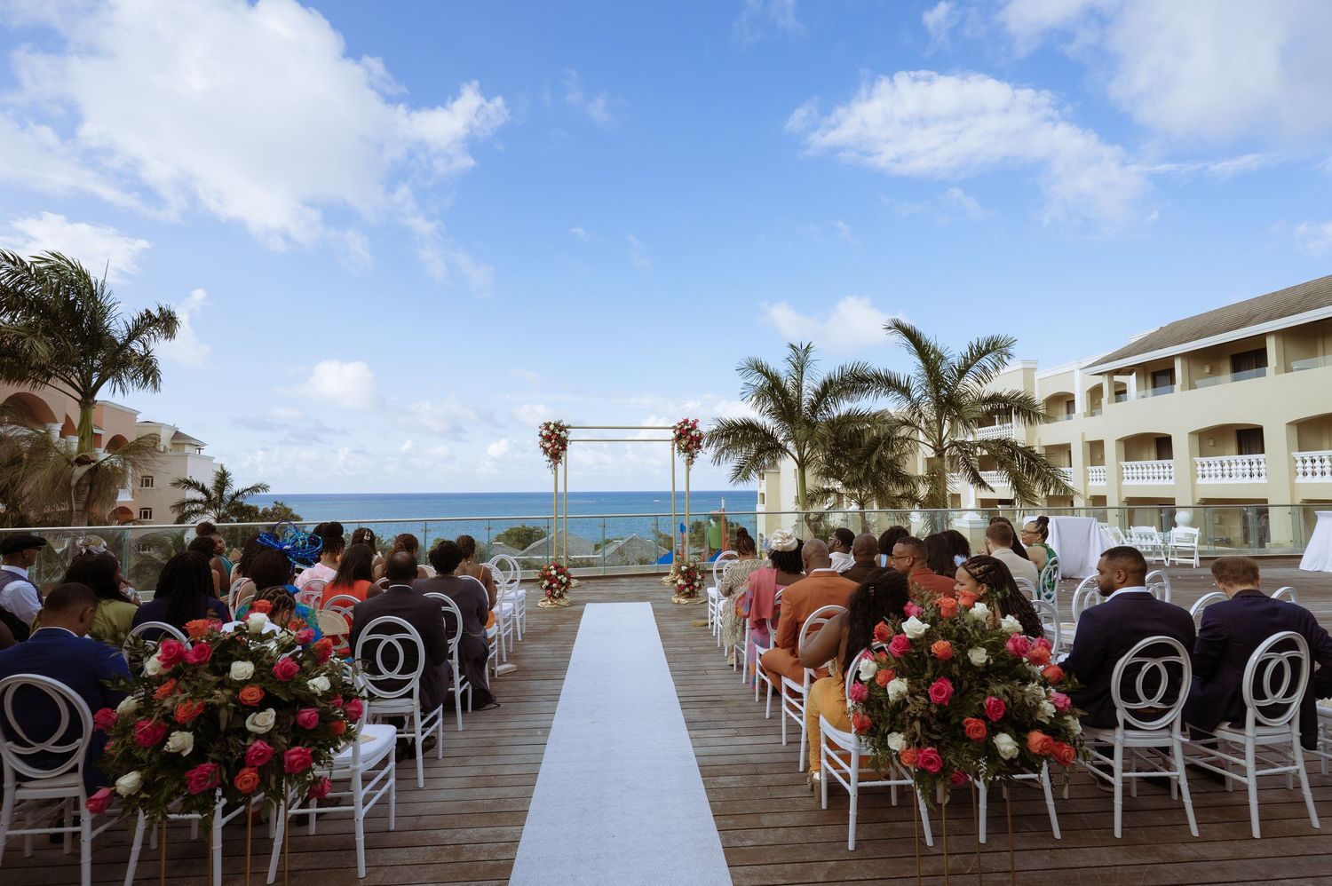 Beachfront wedding ceremony setup with white chairs and red floral arrangements under bright blue Caribbean skies.