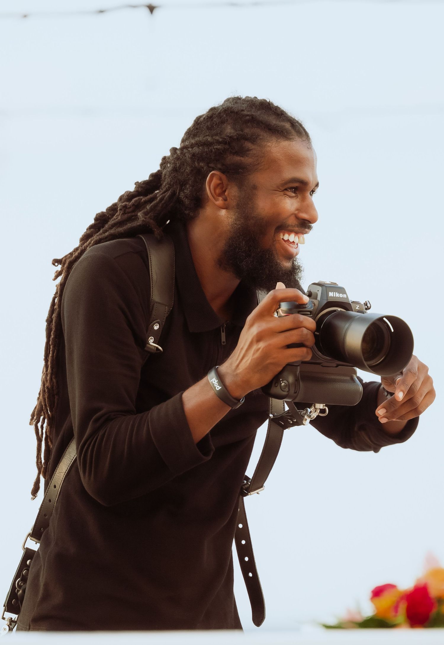 A photographer with dreadlocks wearing a dark jacket takes photos with a professional camera in three sequential shots.