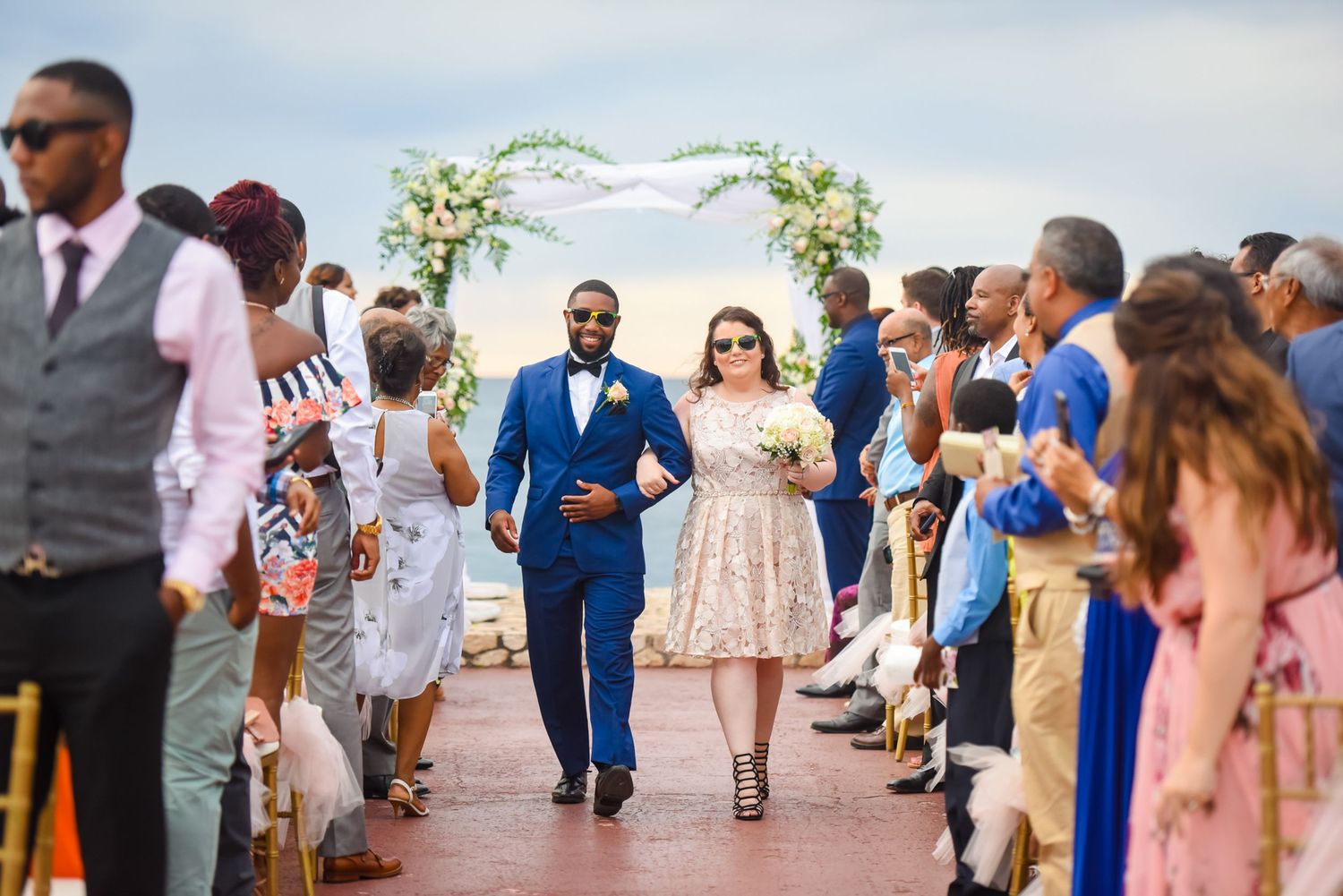 Wedding guests walking down aisle at outdoor beach ceremony.