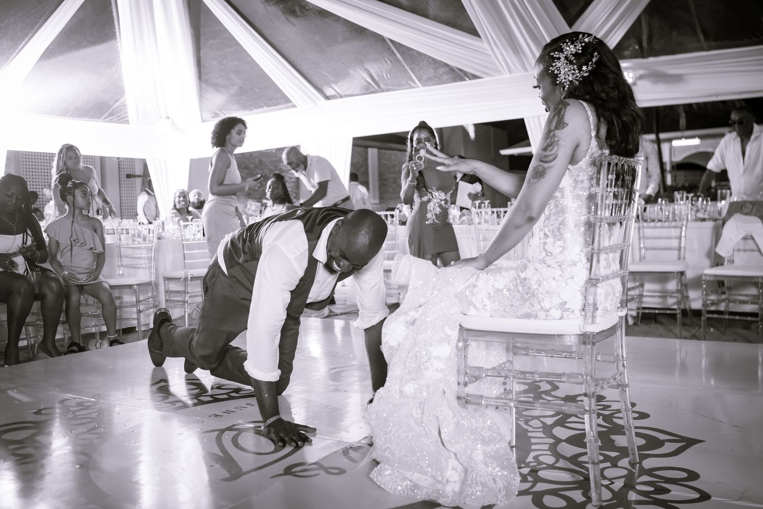 A black and white photo captures wedding guests dancing on an illuminated dance floor.